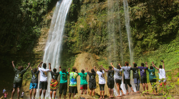 Group of people with hands held high facing a waterfall