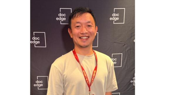 Filmmaker Daniel Lin stands before Doc Edge film festival backdrop.