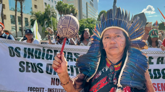 An Indigenous woman protesting or advocating for Indigenous rights at a public event with a sign.