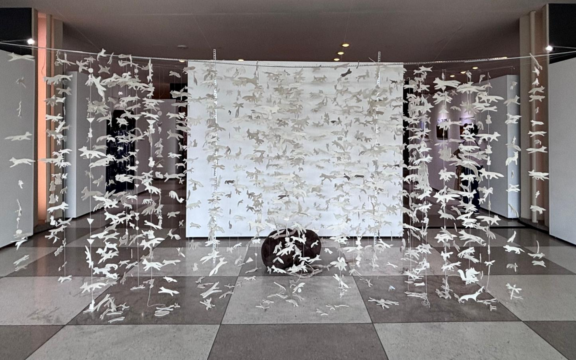 Hundreds of palm-sized felt white-colored foxes hang from 6-foot high wire. A large rock sits in the center of the exhibit covered in the white felt foxes.