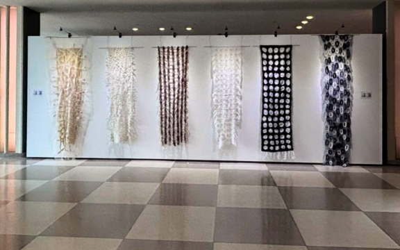 A series of six rectangular felt and silk panels in black, white and cream hang from a pole