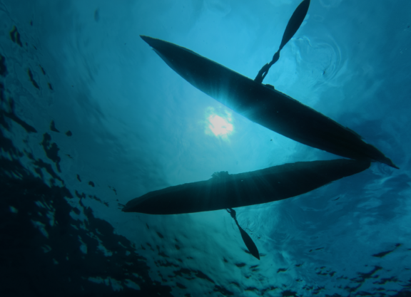 Indigenous canoes floating on the water's surface, viewed from beneath the blue ocean.