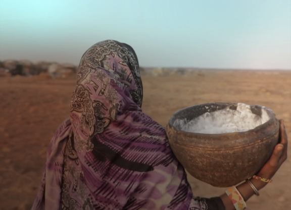 An Indigenous woman carrying a clay bowl, seen from behind.